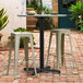 A Lancaster Table & Seating black outdoor table base with 3 bar stools on a brick patio.