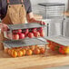 A man holding a stack of Vigor clear food pans filled with fruit.