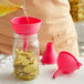 A person using a pink Fox Run silicone funnel to pour liquid into a jar.