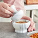A person grinding spices in a white marble mortar on a counter.