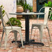 A black Lancaster Table & Seating Excalibur outdoor table base with a white table and chairs on a brick patio.