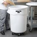 A man pouring pasta into a large white Rubbermaid storage container with a black lid.