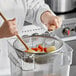 A hand using a Choice stainless steel strainer to stir a bowl of vegetables.