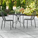 A Lancaster Table & Seating Harbor black outdoor table with two chairs on a patio.