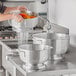 A person washing vegetables in a Choice aluminum colander on a counter.