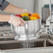 A person holding a Choice aluminum colander full of peppers over a sink.