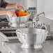 A person washing vegetables in a Choice heavy-duty aluminum colander.