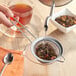 A person pouring tea into a Choice stainless steel fine mesh strainer.