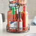 A bottle of hot sauce sits in a black wrought iron condiment caddy on a table.