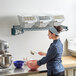 A woman mixing ingredients in a blue bowl on a white surface using a Baker's Lane ingredient bin shelf.