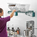 A woman in purple scrubs putting ingredients on a Baker's Lane wall-mounted shelf.