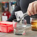 A person using tongs to add a red silicone ice cube to a drink.