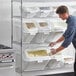 A man putting food into white Baker's Lane shelf bins.