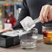 A person using tongs to add a Choice Black Silicone 2" cube ice to a glass.