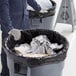 A man in a blue coverall holding a black Lavex Hercules trash bag.