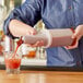 A person using a Choice plastic pour bottle with a brown spout to pour a drink into a glass.