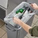 A person putting a Lavex Hercules trash bag full of bottles into a trash can.