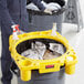 A man in a yellow uniform holding a Lavex Hercules yellow and black trash bag over a yellow garbage can.