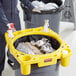 A man in a yellow shirt and black pants holding a yellow Lavex Hercules trash bag over a yellow garbage bin.