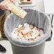 A person holding a tray of food with a fork and knife dumping it into a trash can lined with a Lavex Hercules clear trash bag.