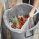 A woman putting a Lavex Li'l Herc trash bag into a trash can.