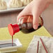 A person's hand pouring Town Round Red Top Soy Sauce from a glass jar into a bowl of dumplings.