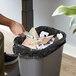 A person putting a Lavex black garbage bag into a black trash can.