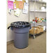 A grey trash can with a black Lavex Hercules can liner sitting next to a shelf in a room.