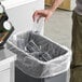 A man putting a clear plastic Lavex trash bag into a trash can full of empty glasses.