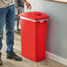 A man in jeans putting a plastic bag into a red Lavex Slim Rectangular Recycle Bin.