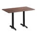 A rectangular standard height table with a textured walnut finish top and two black metal end base plates.