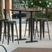 A Lancaster Table & Seating rectangular bar height table with a textured walnut surface and two outdoor base plates on an outdoor patio.