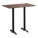 A rectangular bar height table with a textured walnut finish top and two black metal end base plates.