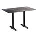 A rectangular table with a dark, smooth finish top and two black metal pedestal bases.