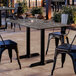 A rectangular outdoor dining table with a smooth dark stone-like finish and two sturdy black metal base plates, surrounded by black metal chairs.