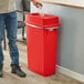 A man in a corporate office cafeteria throwing a plastic bottle into a red Lavex slim rectangular trash can.