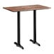 A rectangular bar height table with a textured Yukon oak finish top and two black metal end base plates.