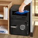 A hand using the electronic keypad to open a black steel depository safe.