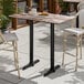 A rectangular bar height table with a textured mixed plank finish and two black metal end base plates, designed for outdoor use.