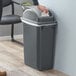 A woman using a Lavex Slim Rectangular Trash Can with dome swing lid to dispose of a tissue in a corporate office cafeteria.