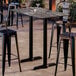 A rectangular bar height table with a smooth dark finish and two sturdy black base plates, designed for outdoor use.