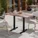 A rectangular standard height table with a textured mixed plank finish and two black end outdoor base plates.