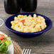 A close up of a Tuxton cobalt blue monkey dish filled with macaroni and cheese on a table with a salad.