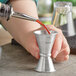 A person using a Tablecraft stainless steel Japanese jigger to pour liquid into a metal cup.