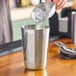 A person pouring ice into a Tablecraft stainless steel cocktail shaker tin.
