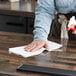 A person using a spray bottle to clean a table in a professional kitchen with a WypAll X80 foodservice wiper.