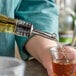 A person using a Tablecraft stainless steel free flow liquor pourer to pour liquid into a glass on a counter.