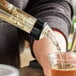 A person using a TableCraft clear liquor pourer to pour liquid into a glass on a counter.