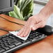 A hand wiping a keyboard with a Kimtech Kimwipe.