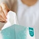 A woman holding a Kleenex Naturals Professional tissue box with a tissue in it.